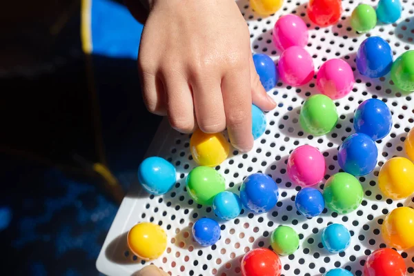 stock image Baby plays with colourful mosaics on white surface. Kids hand with bright constructor for developing creativity and motor skills. Early education. Puzzle for preschoolers. Fingers with toy in sunlight