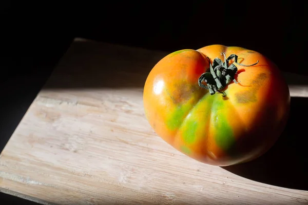 新鲜多汁的红色西红柿 绿色斑点 与伦勃朗的阳光相反 一个孤立的蔬菜在木制表面的黑色背景 生物素食无麸质营养概念 — 图库照片