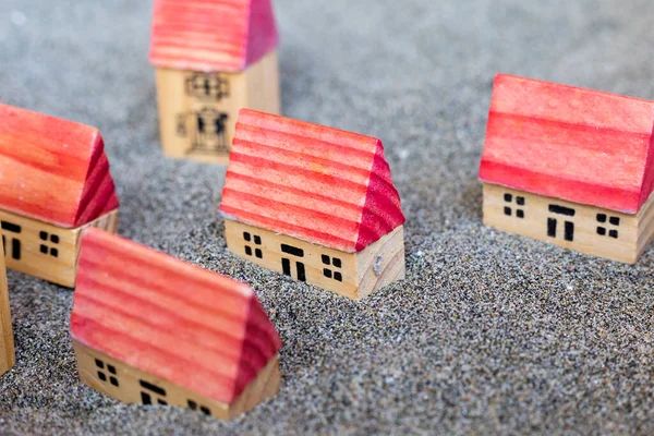Small wooden toy houses. Building homes on sand. Children game. Five cottages with red roof on grey soil. Modelling village. Construction and architectural concept. City in miniature. Creativity