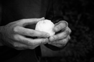 Monokrom kompozisyonu. Adam el ele tutuşmuş portakal meyvesi soyuyor. Parmaklar beyaz yuvarlak ürüne dokunur. Yüksek kontrastlı kompozisyon. Sağlıklı gıda konsepti.