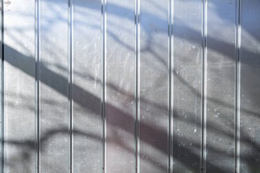 Bu metal bir çitin yakın plan görüntüsü, yüzeyin altında belirgin bir gölge bırakıyor, olay yerine derinlik katıyor.