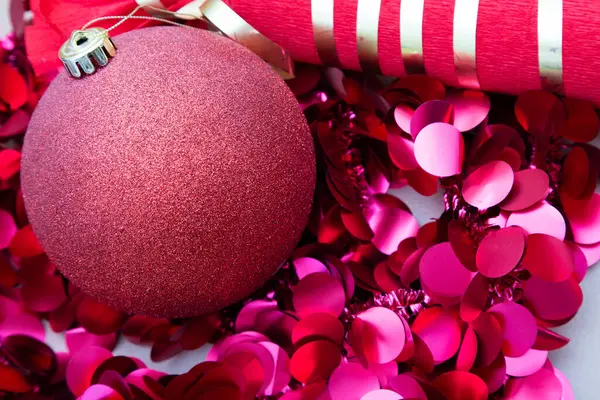 Hoş pembe bir Noel süsü, neşeli pembe konfeti bolluğuyla güzelce çevrelenmiş ve şenlikli atmosfere eklenmiştir.