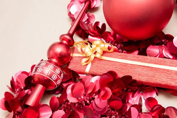 Canlı kırmızı bir Noel süsü güzelce paketlenmiş kırmızı bir hediye kutusunun üstüne yerleştirilir ve şenlik havası katar.