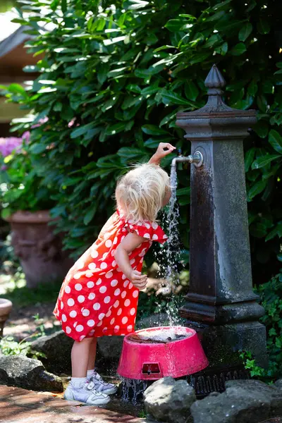 Küçük bir kız bahçede sıcak bir günde güzel bir çeşmeden ferahlatıcı bir su içiyor.