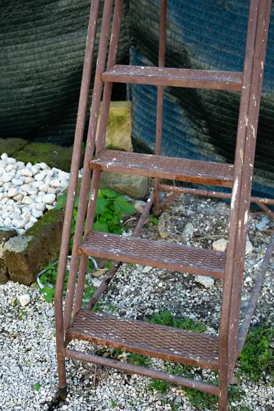 Paslı ve yıpranmış metal bir merdiven çamurda boş boş oturuyor, yıpranmış görünümünü ve açık havada zamanın akışını gösteriyor.