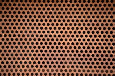Detaylı bir yakın çekim görüntüsü delikli metal bir yüzey sergiliyor. Bu yüzey boyunca sayısız siyah nokta aynı şekilde dizilmiş.