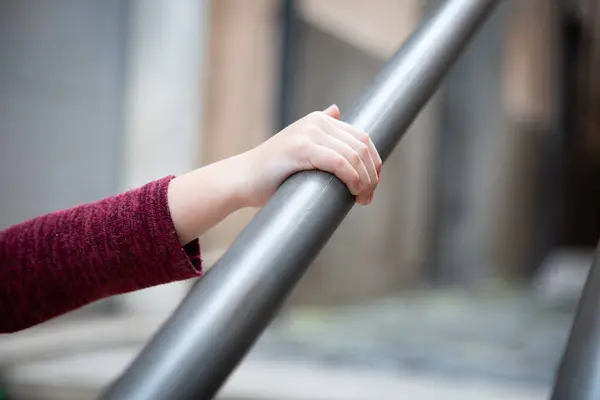 Bir insan eli sağlam bir metal korkuluğu sıkıca kavrıyor, etrafındaki boşlukta gezinirken güvenlik ve istikrarı sağlıyor.