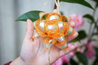 Bir insan elinde canlı turuncu ve beyaz bir fiyonk tutuyor. Tasarım ve işçiliğinin karmaşık detaylarını gösteriyor.