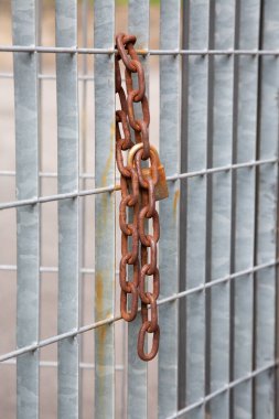 Paslı bir zincir, eskimiş ve yıpranmış metal bir çitten sarkıyor, zamanla aşınma ve yırtılma izleri gösteriyor.