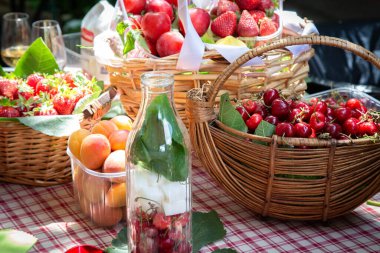 Taze meyve dolu renkli sepetlerle süslenmiş güzel bir piknik masası ve ferahlatıcı bir şişe su var.