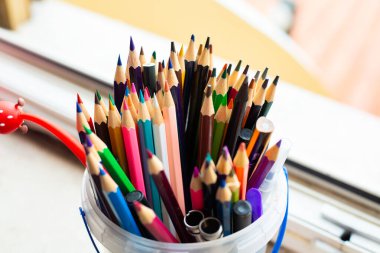 Renkli kalemler ve makaslarla ağzına kadar doldurulmuş canlı bir plastik kova.