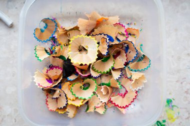 Ağzına kadar dolgulu ve renkli kalem talaşlarıyla dolu olan plastik bir kap, çeşitli gölgeler ve renkler sergiliyor.