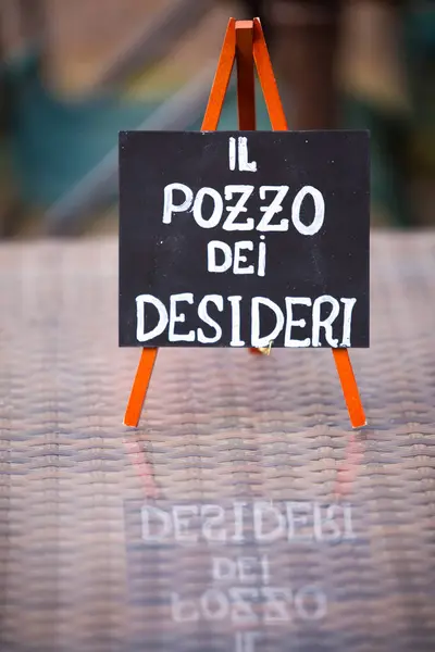İl pozzo dei desideri yazan bir sehpada çok güzel hazırlanmış bir tabela. İngilizce dilek kuyusuna tercüme ediliyor.