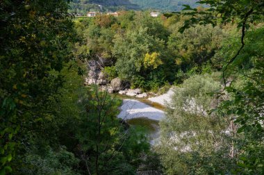 Bereketli, yeşil ağaçlar sığ, dolambaçlı bir nehir olan Natisone 'u saran kayalık, çakıl dolu bir yatak.