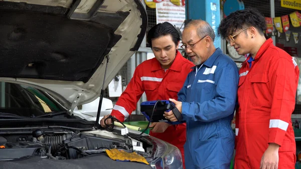 senior asian car mechanic manager training apprentice to checking car engine by Diagnostics Software repair in garage . old asia Auto mechanic teaching trainee or assistant on the repair shop .