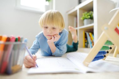 İlkokul öğrencisi evde ödev yapıyor. Çocuk saymayı öğreniyor, çalışma kitabında aritmetik örnekleri çözüyor. Matematik dersi. Anaokulu bebeğini okula hazırlıyorum. Çocuklar için eğitim