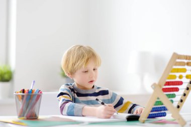 İlkokul öğrencisi evde ödev yapıyor. Çocuk saymayı öğreniyor, aritmetik örnekler çözüyor, çalışma kitabı alıştırmaları yapıyor. Matematik dersi. Anaokulu bebeğini okula hazırlamak. Çocuklar için eğitim.