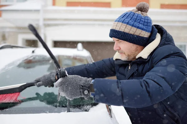 雪の後にブラシを使用して成熟した男のクリーニング車 自動車のフードに吹雪の後の雪のドリフト 雪嵐の後 都市の道路上の困難な交通状況 冬の天候特定 — ストック写真