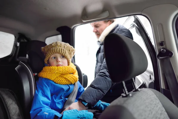 中世の父は 彼の就学前の息子が車の座席にシートベルトを固定するのを助けます かわいい子供は冬の日に車の中に座っています 児童の輸送に関する保安規定 — ストック写真