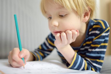 İlkokul öğrencisi evde ödev yapıyor. Çocuk saymayı öğreniyor, aritmetik örnekler çözüyor, çalışma kitabı alıştırmaları yapıyor. Matematik dersi. Anaokulu bebeğini okula hazırlamak. Çocuklar için eğitim.