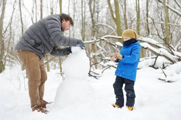 小男孩和他的父亲在雪地公园里堆雪人 冬天与有孩子的家庭一起积极地进行户外活动 父母和孩子在雪地的冬日公园里散步 — 图库照片