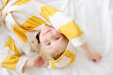 Bornozlu küçük bir çocuğun portresi uyandıktan sonra yatakta yatar. Ev için çocuk kıyafetleri. Çocuk sabah rutini yapıyor ve anaokuluna gitmeye hazırlanıyor. Tembel bebek yataktan çıkmak istemiyor..