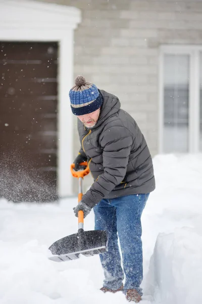 Mature man clean path near house from snow during strong blizzard. Person shoveling snow out of driveway. Huge snowdrifts. Difficult situation in the city after a snow storm. Winter weather specific.