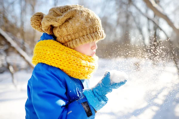 小さな男の子が手から雪を吹いていた 子供たちは雪の日に公園を歩くのを楽しむ 雪の中で楽しい赤ちゃん 子供連れの家族のための屋外冬の活動 — ストック写真