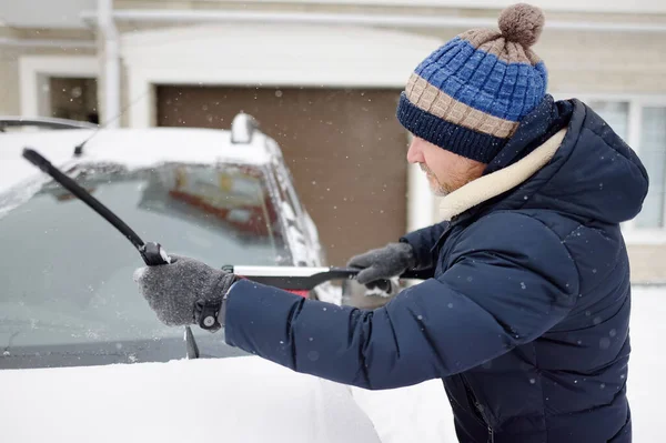 雪の後にブラシを使用して成熟した男のクリーニング車 自動車のフードに吹雪の後の雪のドリフト 雪嵐の後 都市の道路上の困難な交通状況 冬の天候特定 — ストック写真