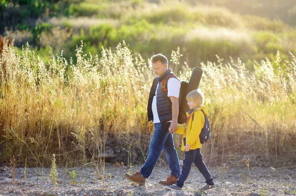 Cute schoolchild and his mature father hiking together and exploring nature. Child learning survival skills and orienteering. Concepts of adventure, scouting and hiking tourism for kids.