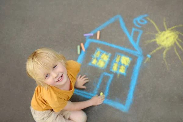 小さな子供の男の子の家や太陽の歩道のアスファルトの上に色のチョークで塗装描画されます 道路の灰色の背景に子供の創造的な画像 世界中の家庭と平和な生活の概念 — ストック写真