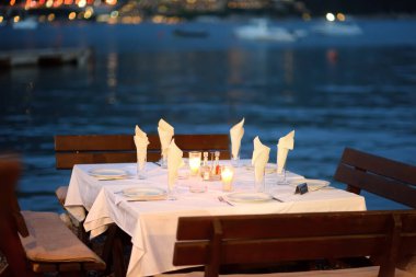 Alacakaranlıkta deniz kıyısında boş bir Avrupa kafesi. Yanan bir mumla şık bir masa dekorasyonu. Rıhtımdaki açık hava restoranı. Boş bir masa..