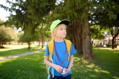 Beyzbol şapkalı, sırt çantalı ve yaka kartlı ilkokul öğrencisi okula gidiyor. Çocuk okul otobüsünü bekliyor. Çocuklar için eğitim.