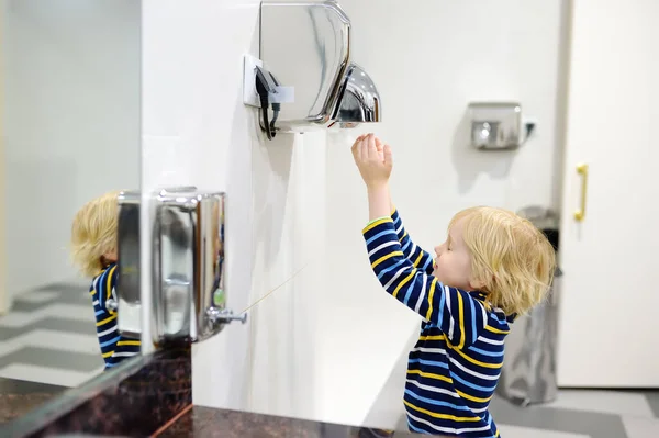 Child using restroom. Little boy dries his hands in the toilet with an automatic dryer. Taking care of the hygiene of children in public places. Healthy habits for kids