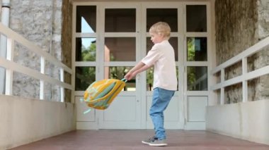 A little student boy is spinning and jumping with a backpack at the door of the school building. Happy child has fun after finishing the lessons. Back to school