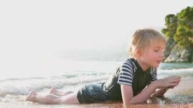 Mutlu çocuk dalgalarda uzanıyor ve ılık deniz suyunun tadını çıkarıyor. Neşeli çocuk deniz kıyısındaki bir plaj tatilinde eğleniyor. Okul tatilinde çocuklar ve tüm aile için boş zaman.