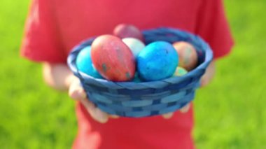 Little boy holding a blue straw basket full of colorful eggs after Easter hunt in spring garden. Traditional festival outdoors. Child celebrate Easter holiday.