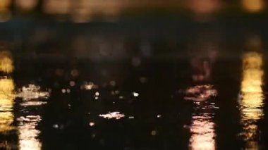 Bir gecede yağmur fırtınasının atmosferik videosu. Şiddetli yağmur ve alçak noktadan alınan su birikintilerinden geçen arabalardan sıçrama. Sokak lambalarının ışığında büyük damlalar kaldırıma düşer.