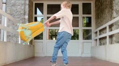 A little student boy is spinning and jumping with a backpack at the door of the school building. Happy child has fun after finishing the lessons. Back to school