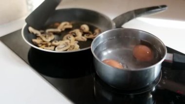 Orta yaşlı bir adamın kahvaltı hazırlarken çekilmiş yakın çekim videosu. Küçük bir tencerede haşlanmış yumurta ve sağlıklı bir yemek için kızarmış mantar.