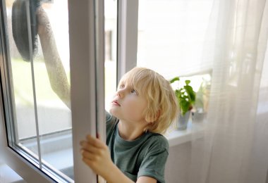 Cute little boy washing a window at home. Child helping parents with household chores, for example, cleaning windows in his house. Children doing housework. Kids household duties