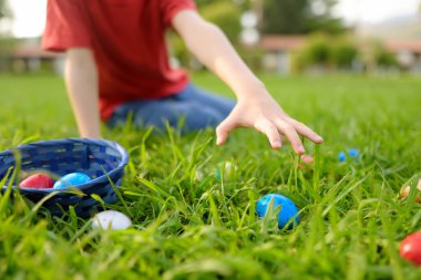 Little boy hunting for multicolor eggs in spring garden on Easter day. Traditional festival outdoors. Child celebrate Easter holiday. Focus on hand.