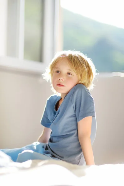 阳光明媚的早晨 卧室里穿着蓝色T恤的可爱的梦幻般的学童的垂直肖像 十多岁的男孩坐在床上做梦 — 图库照片