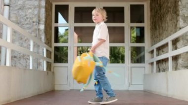 A little student boy is spinning and jumping with a backpack at the door of the school building. Happy child has fun after finishing the lessons. Back to school