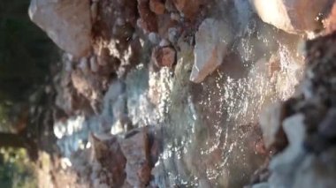 Taşlar arasında akan bir dağ nehrindeki en saf şeffaf suyun dikey videosu. Dağlarda güneşli bir günün detayları. Dağdaki pınarda saf temiz su.