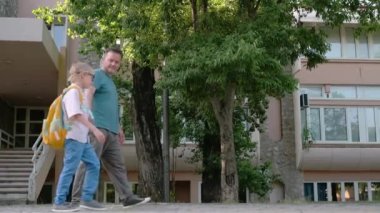 An elementary school student walks from school accompanied by his middle-aged father. A boy tells his dad how his school day went on the first day after the holidays. Primary school pupil with parents