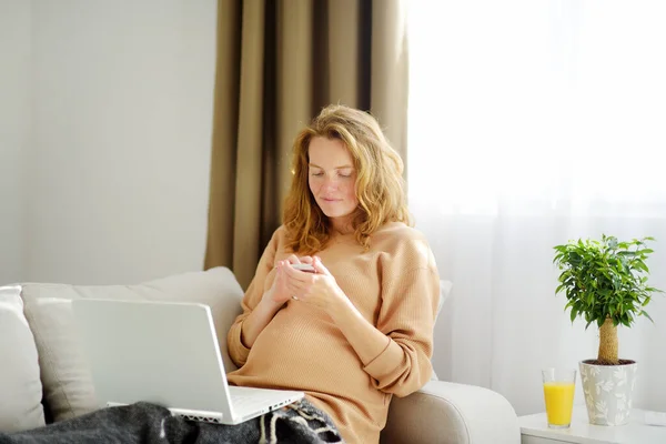 年轻的孕妇在家庭办公室的电脑上工作 准妈妈在远程工作或在社交网络上聊天时 会在电话上留言 保持联络受孕 — 图库照片