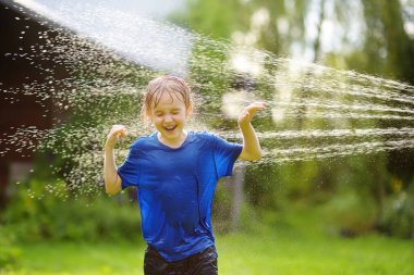 Funny little boy playing with garden sprinkler in sunny backyard. Preschooler child laughing, jumping and having fun with spray of water. Outdoors activity for kids on hot summer day