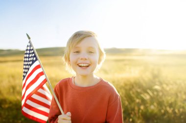 Cute little boy celebrating of July, 4 Independence Day of USA at sunny summer sunset. Child running with american flag of United States on wheat field. Proud little american boy holding country flag