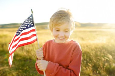 Cute little boy celebrating of July, 4 Independence Day of USA at sunny summer sunset. Child running with american flag of United States on wheat field. Proud little american boy holding country flag
